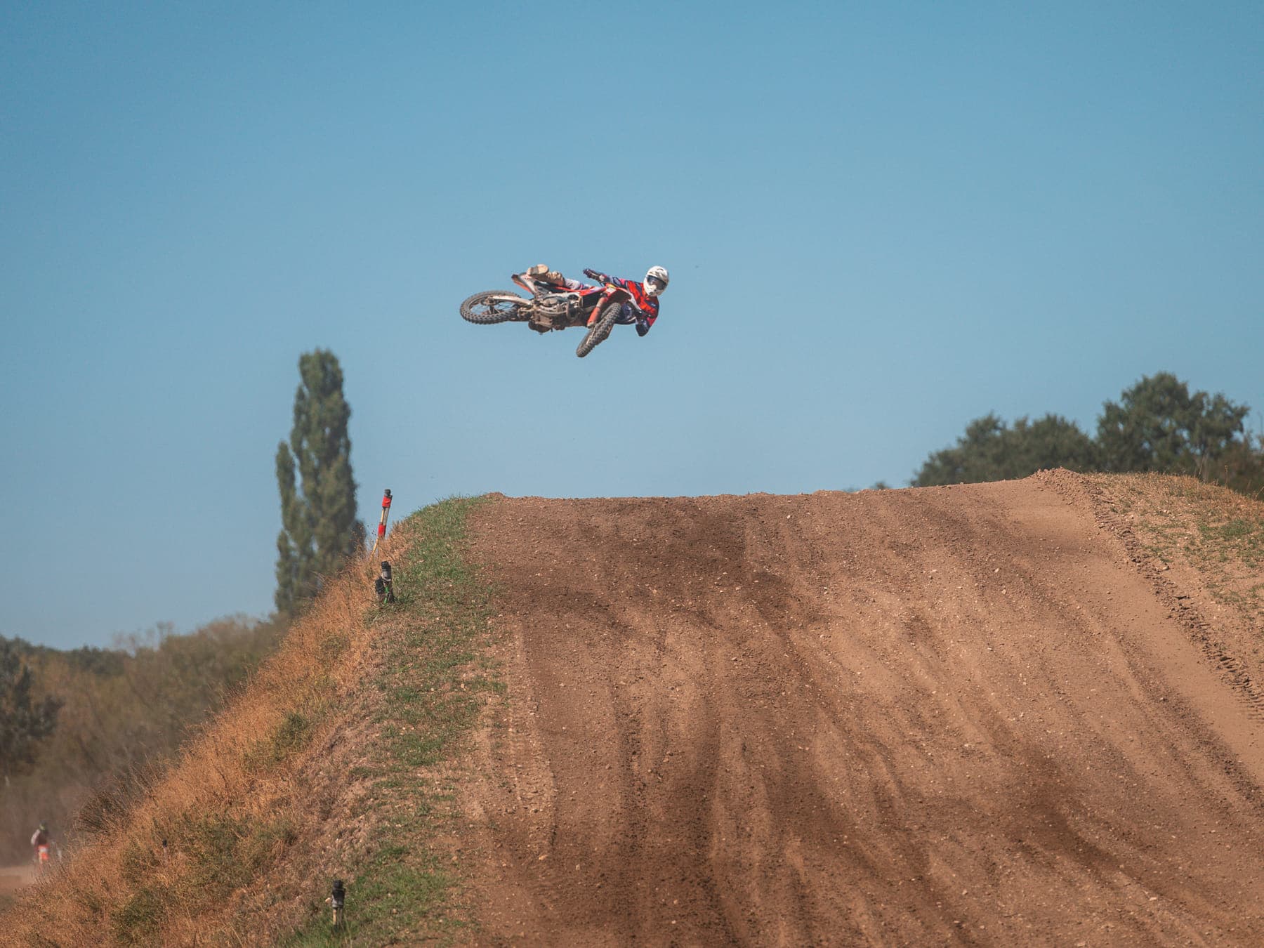Motocross-Fahrer quer in der Luft über der großen Sprungschanze vor blauem Himmel