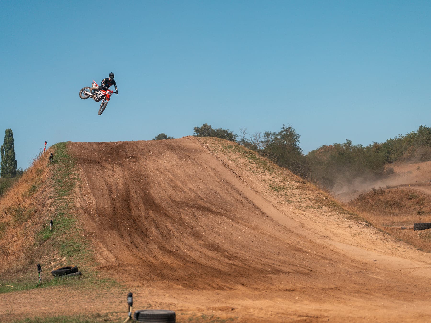 Fahrer im Sprung über den großen Erdhügel der Motocross-Strecke, von der Seite